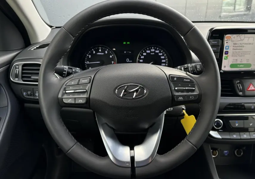 Vue intérieure centrée sur le volant cuir noir de la Hyundai i30 SW T-GDI 120 Modern avec tableau de bord et écran tactile.