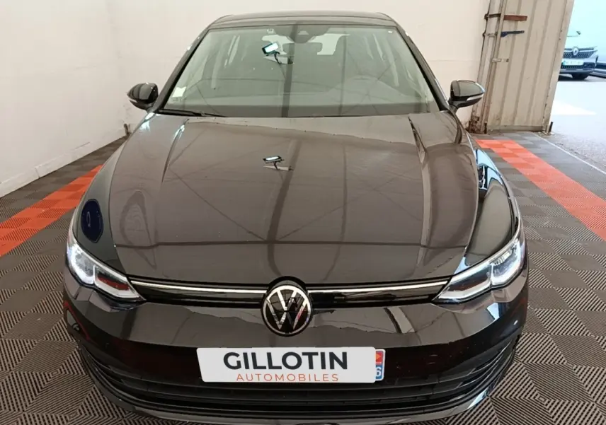 Vue frontale d'une Volkswagen Golf noire 2023 avec phares LED et calandre chromée dans un garage.