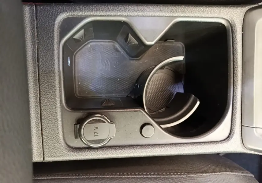 Vue rapprochée de la console centrale noire d’une Volkswagen Golf 2023, avec prise 12V et zone de recharge sans fil.