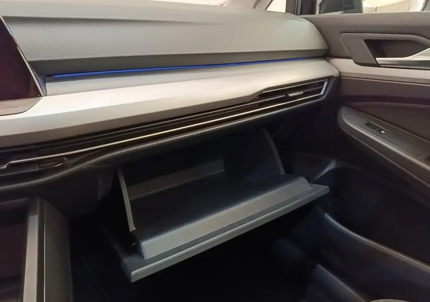 Intérieur de la Volkswagen Golf 2.0 TDI 2023, vue côté passager sur la boîte à gants ouverte et tableau de bord noir avec éclairage bleu.