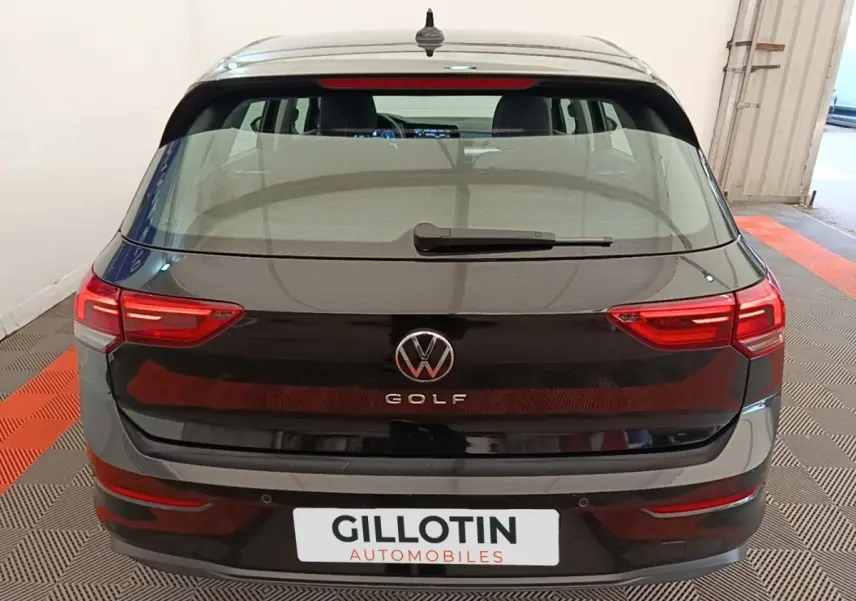 Vue arrière d'une Volkswagen Golf noire 2023 avec feux LED et logo central visible en intérieur showroom.
