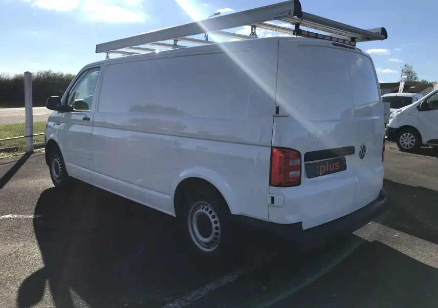 Vue 3/4 arrière droite d'un Volkswagen Transporter blanc équipé d'un porte-échelle sur le toit, stationné en extérieur.