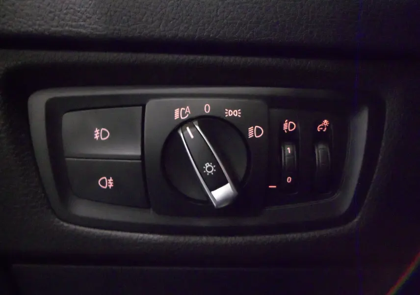 Gros plan sur le panneau de commande des phares de la BMW Série 1 F21 LCI 118i gris, avec réglages lumineux éclairés.