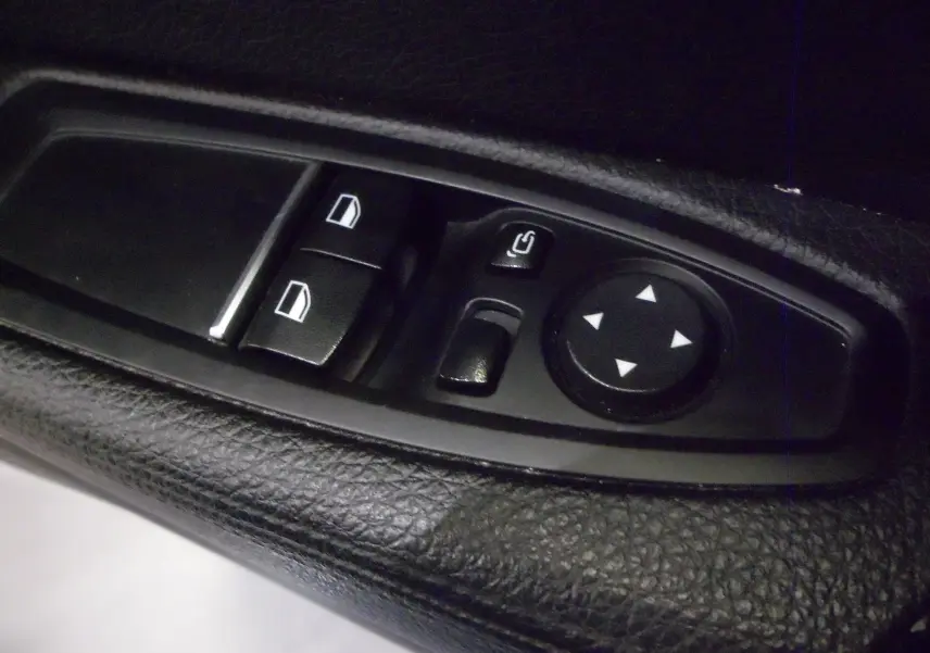 Gros plan sur les commandes de réglage des vitres et des rétroviseurs côté conducteur en cuir noir d'une BMW Série 1 F21 LCI gris.