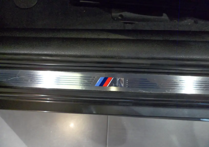 Gros plan sur la plaque de seuil de porte BMW M en métal brossé avec logo tricolore rouge, bleu et bleu clair.