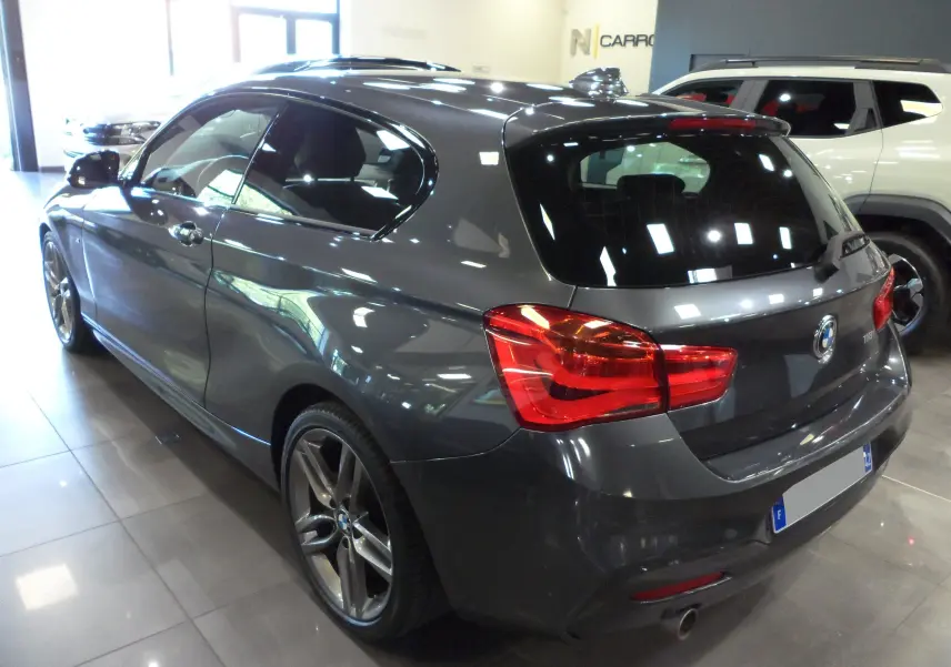 Vue 3/4 arrière droite d'une BMW Série 1 F21 LCI gris métallisé avec jantes alliage et feux arrière LED visibles.