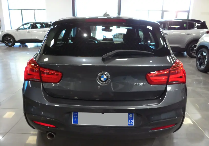 Vue arrière d'une BMW Série 1 F21 LCI gris foncé avec feux rouges allumés dans un showroom lumineux.