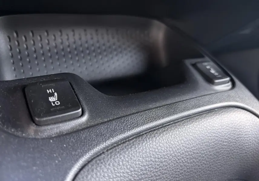Bouton de réglage de siège chauffant en gros plan dans l'habitacle noir d'une Toyota Corolla Hybride 2020.