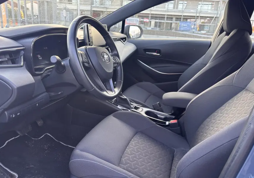 Intérieur de la Toyota Corolla hybride 2020 vu côté conducteur, sièges tissu gris et tableau de bord moderne.