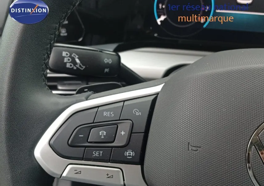 Gros plan sur le volant noir de la Volkswagen Golf VIII avec commandes intégrées et tableau de bord numérique en arrière-plan.