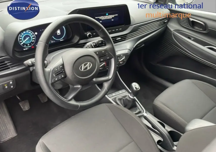 Vue intérieure de face côté conducteur de la Hyundai i20 2025 avec volant cuir noir et tableau de bord digital.