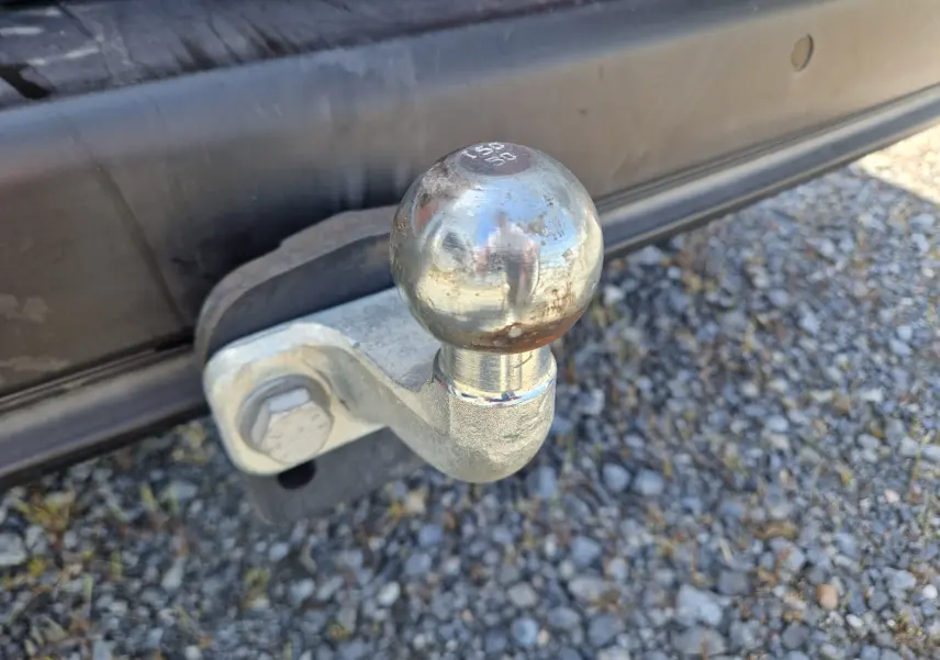 Gros plan sur la boule d’attelage métallique fixée à l’arrière d’un Citroën Berlingo blanc, sur un sol gravillonné.