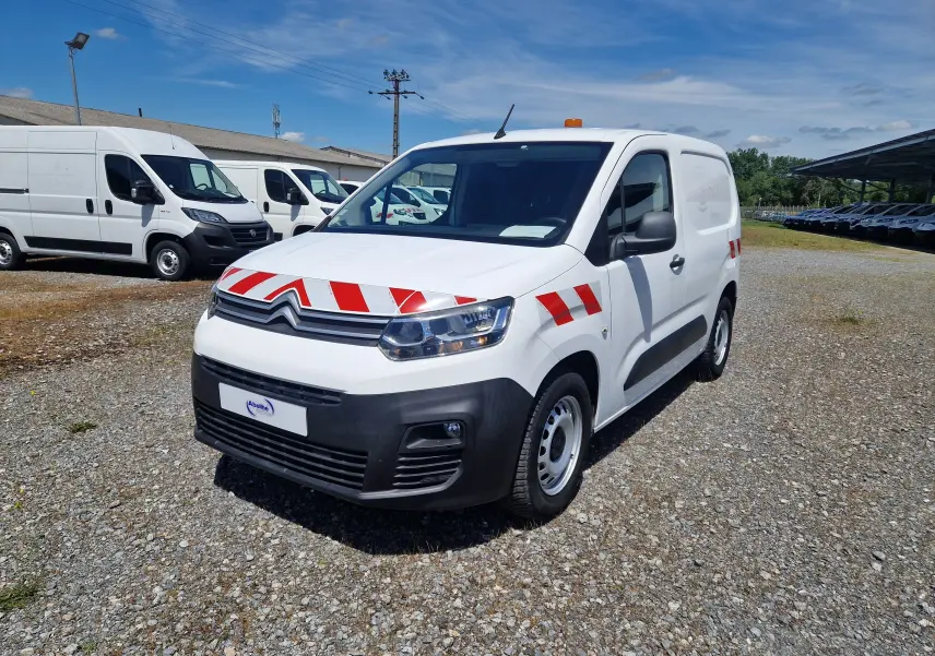 Vue 3/4 avant droit d'un Citroën Berlingo blanc avec bandes rouges réfléchissantes et gyrophare orange sur le toit.