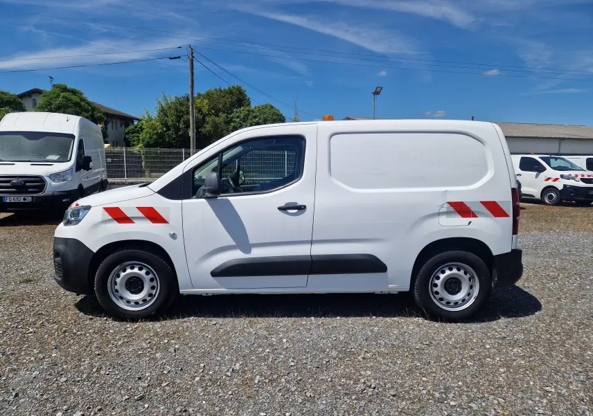Vue latérale droite d’un utilitaire Citroën Berlingo blanc de 2020 avec bandes rouges réfléchissantes et gyrophare orange sur le toit.