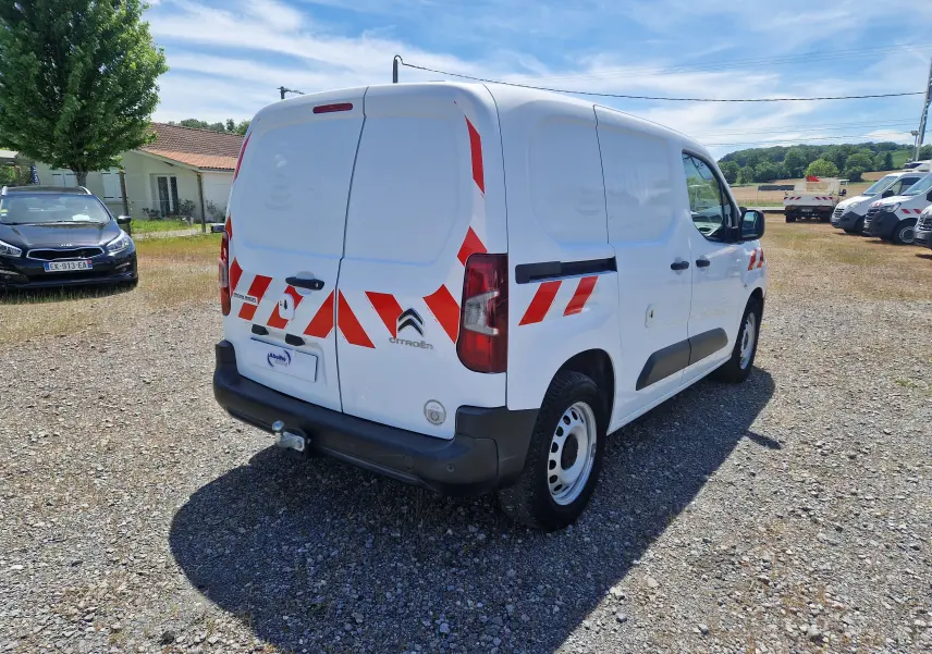 Vue 3/4 arrière droite d’un Citroën Berlingo blanc utilitaire avec bandes réfléchissantes rouges et gyrophare sur le toit.