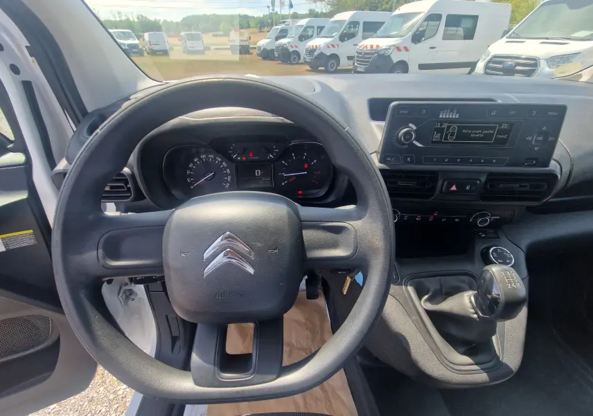 Vue intérieure du poste de conduite du Citroën Berlingo blanc 2020, volant, tableau de bord et levier de vitesses manuel visibles.