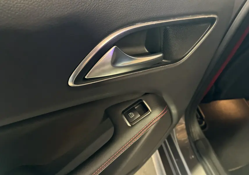 Gros plan sur la poignée intérieure côté gauche en cuir noir avec surpiqûres rouges d'une Mercedes Classe A 250 AMG Sport gris.