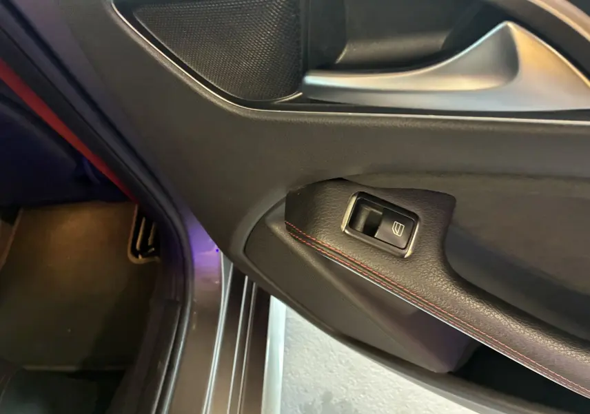 Gros plan sur la commande de lève-vitre côté gauche de la porte intérieure noire avec surpiqûres rouges d'une Mercedes Classe A 250 AMG Sport.