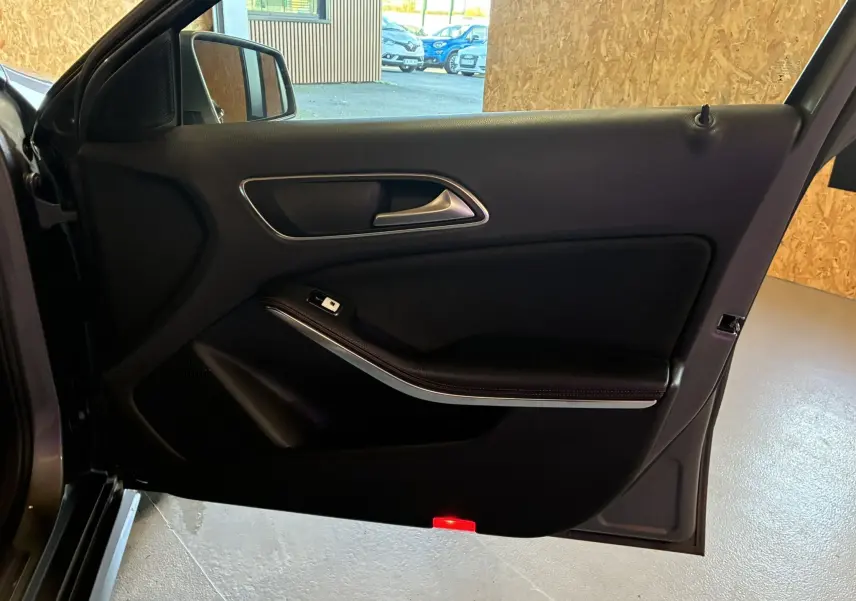 Vue intérieure de la porte avant gauche noire d'une Mercedes Classe A 250 AMG Sport gris, avec poignée argentée et bouton de fenêtre.