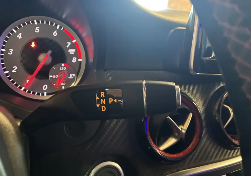 Gros plan intérieur sur le levier de vitesses automatique et les aérateurs rouges d'une Mercedes Classe A 250 AMG Sport gris.