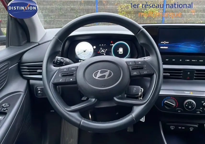 Vue intérieure centrée sur le volant cuir noir d'une Hyundai i20 2025 avec tableau de bord digital et écran tactile.