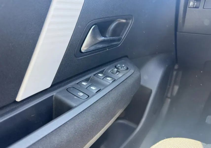 Gros plan sur la commande des vitres électriques côté conducteur d’une Citroën C4 blanche hybride 2025.