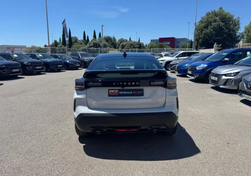 Vue arrière d'une Citroën C4 hybride blanche 2025 avec toit noir, feux arrière LED et double sortie d'échappement.