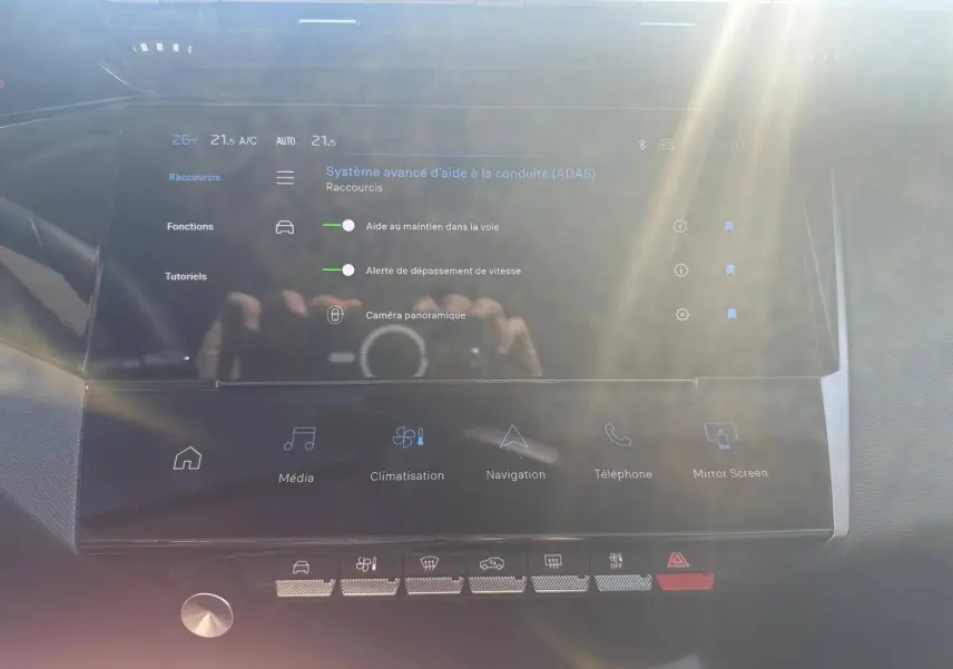 Écran tactile central du Peugeot 308 SW 2025 montrant les aides à la conduite, avec reflets lumineux.