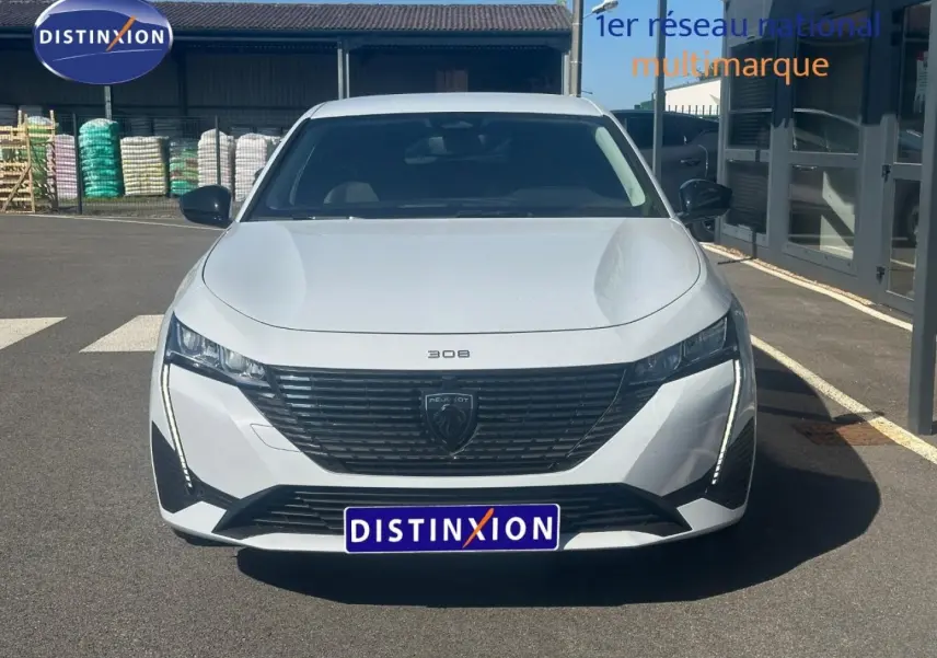 Vue avant d'une Peugeot 308 SW blanche Okénite avec calandre noire et feux LED verticaux allumés.
