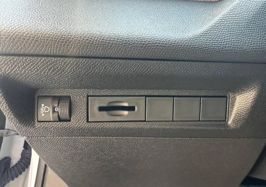 Détail du tableau de bord côté gauche noir texturé avec commande de réglage des phares sur Peugeot 308 SW blanc.