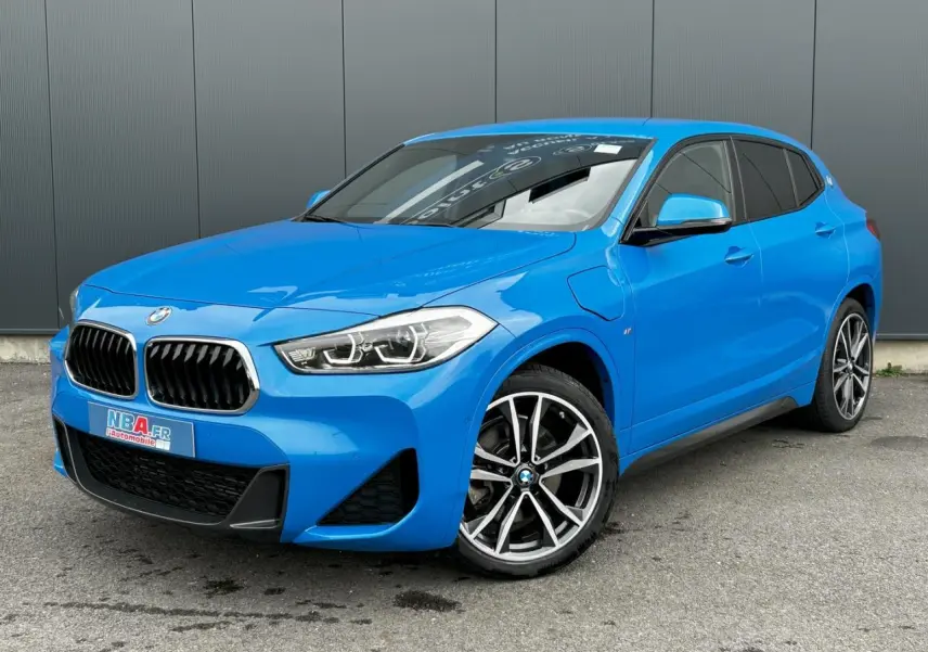 BMW X2 xDrive 25e bleu Misano en 3/4 avant droit, avec jantes alliage bicolores et calandre M Sport visible.