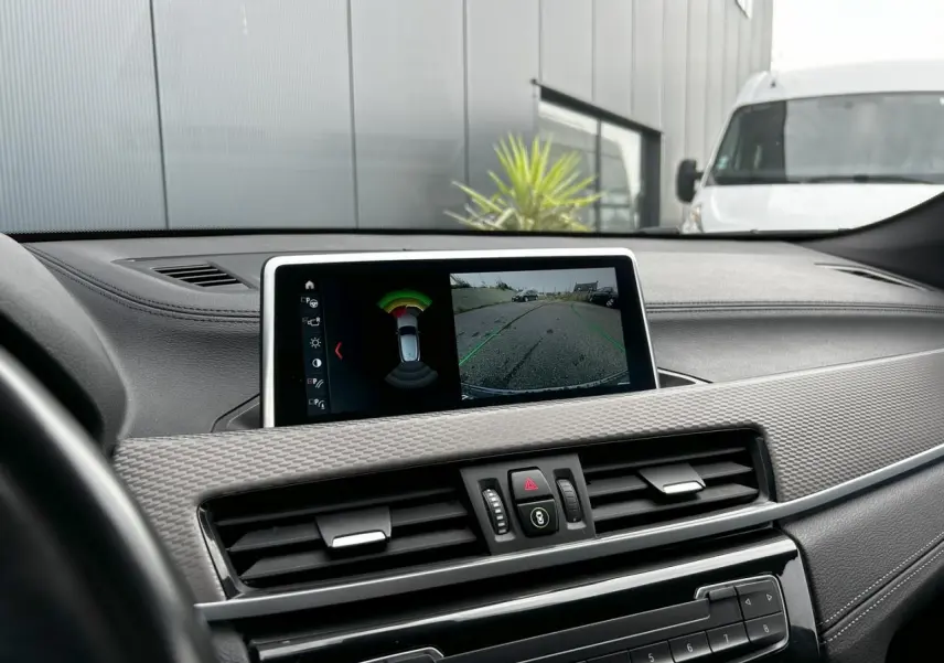 Vue rapprochée du tableau de bord du BMW X2 bleu Misano, avec écran affichant la caméra de recul et les commandes centrales.