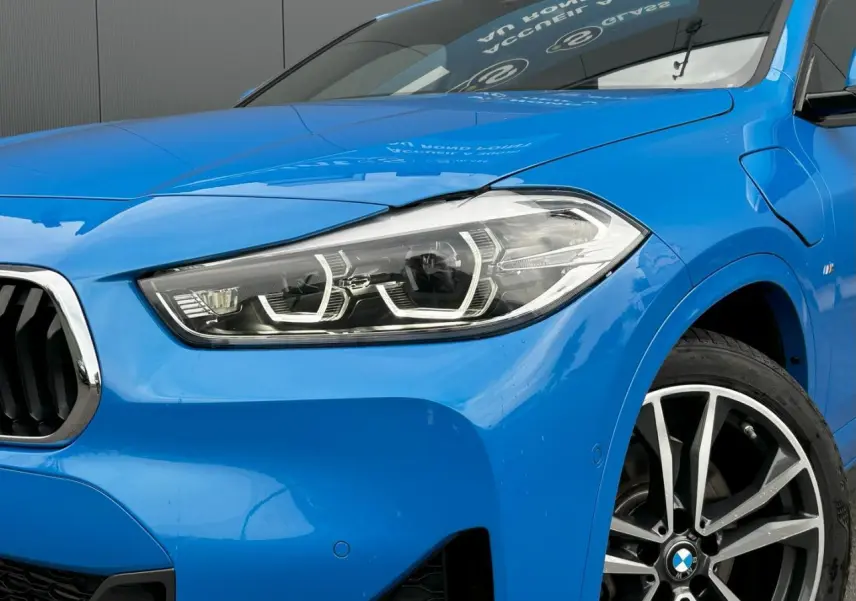 Gros plan sur l'avant droit bleu Misano du BMW X2 F39 avec phare LED et jante alliage bicolore 19 pouces.