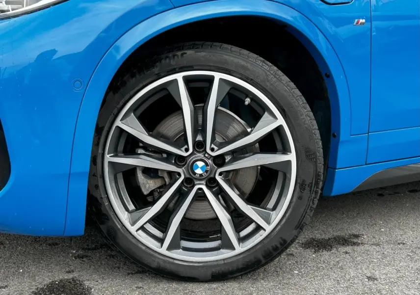 Gros plan sur la jante avant droite bicolore 19 pouces style 919 M d'une BMW X2 bleu Misano avec badge M sur l'aile.