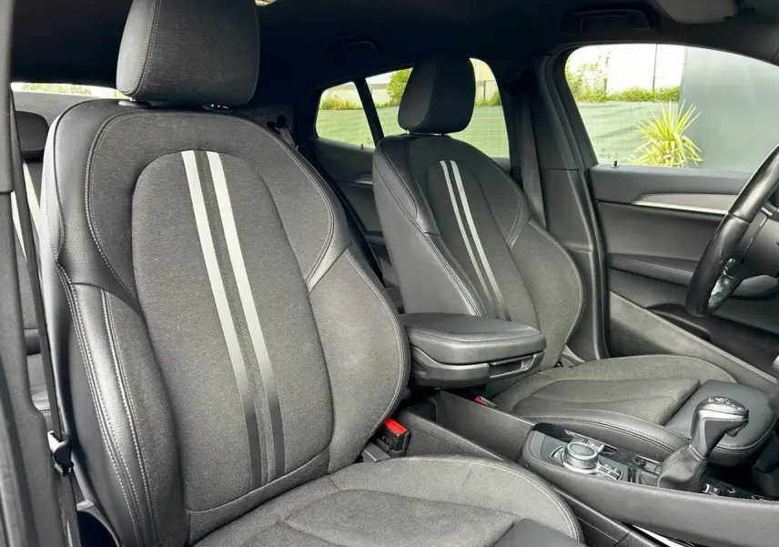 Intérieur avant de la BMW X2 F39 2021, sièges noirs avec bandes grises et accoudoir central visible côté droit.