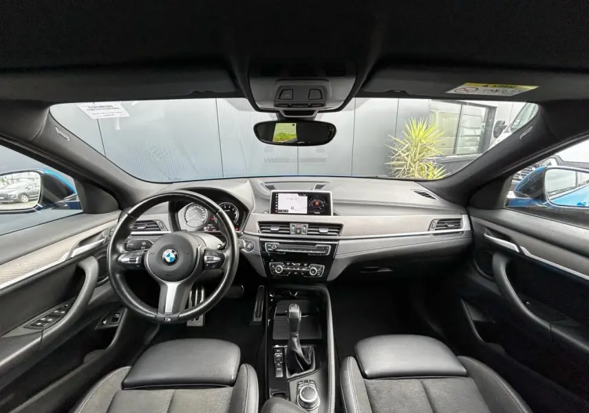 Vue intérieure avant du BMW X2 F39 2021, tableau de bord noir avec volant M cuir et écran GPS central.