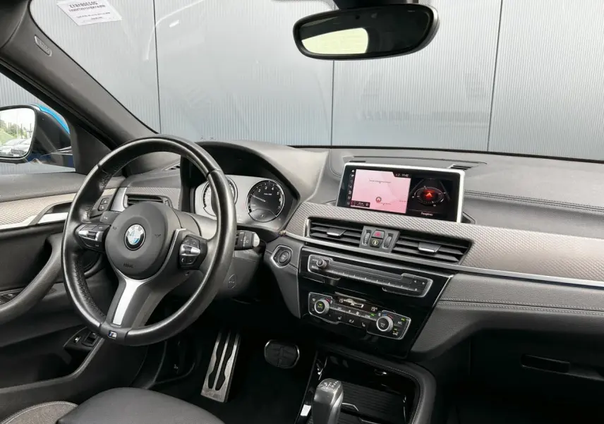 Intérieur avant BMW X2 F39, vue du côté conducteur, tableau de bord noir avec écran GPS et volant cuir M Sport.