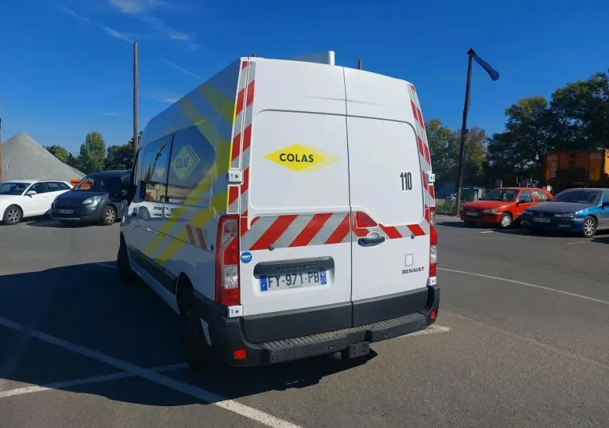 Vue 3/4 arrière droite du Renault Master blanc avec marquages rouges et jaunes Colas, gyrophare et plaque française.