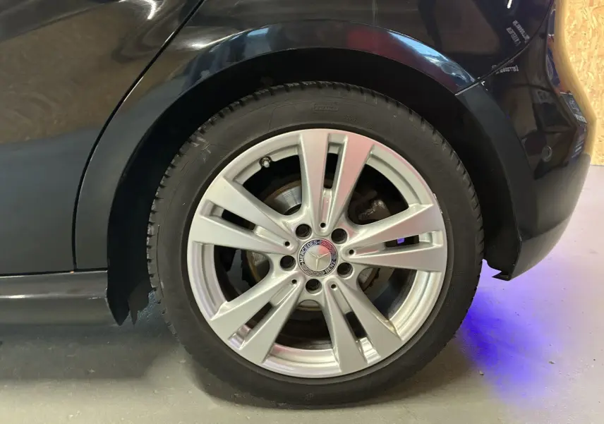 Gros plan sur la roue arrière droite d'une Mercedes Classe A 180 CDI Sensation noire avec jante alliage argentée.