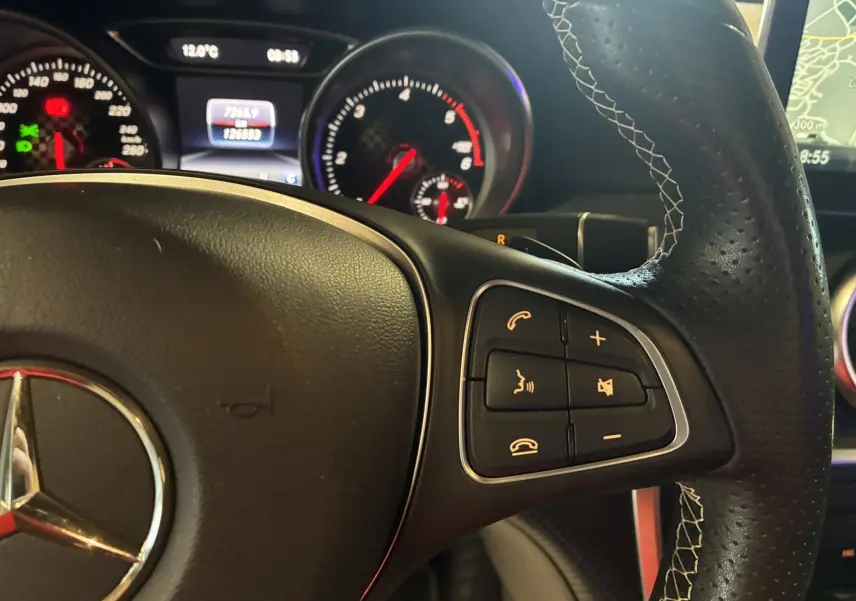 Gros plan sur le volant en cuir noir perforé avec commandes intégrées, tableau de bord et compteur lumineux d'une Mercedes Classe A 180 CDI 2018.