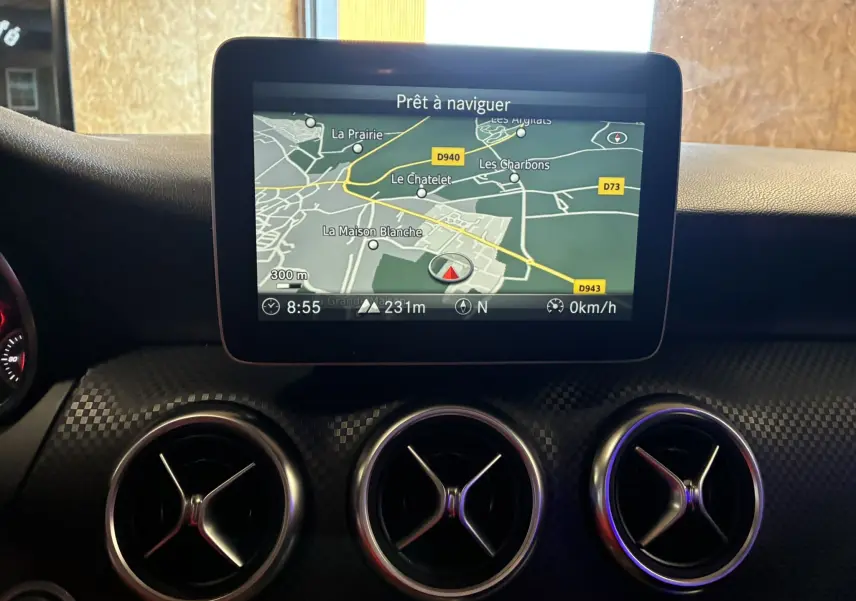Vue rapprochée de l’écran GPS et des aérateurs ronds chromés du tableau de bord noir d’une Mercedes Classe A 180 CDI Sensation 2018.