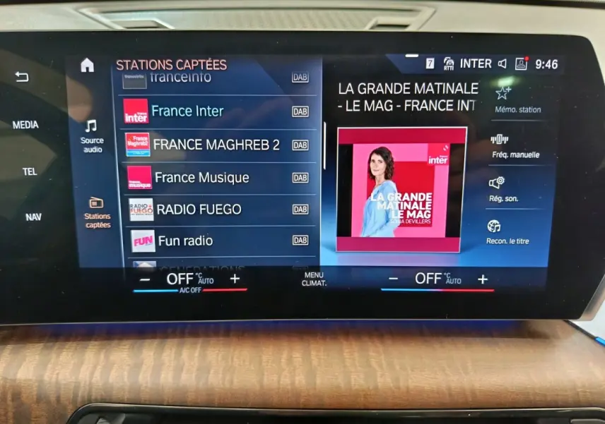 Écran tactile central de la BMW X1 2023 noir, affichant les stations radio et commandes climatisation sur tableau de bord bois.