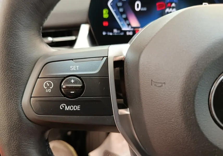 Gros plan sur le côté gauche du volant cuir noir de la BMW X1 2023 avec commandes de régulateur de vitesse.