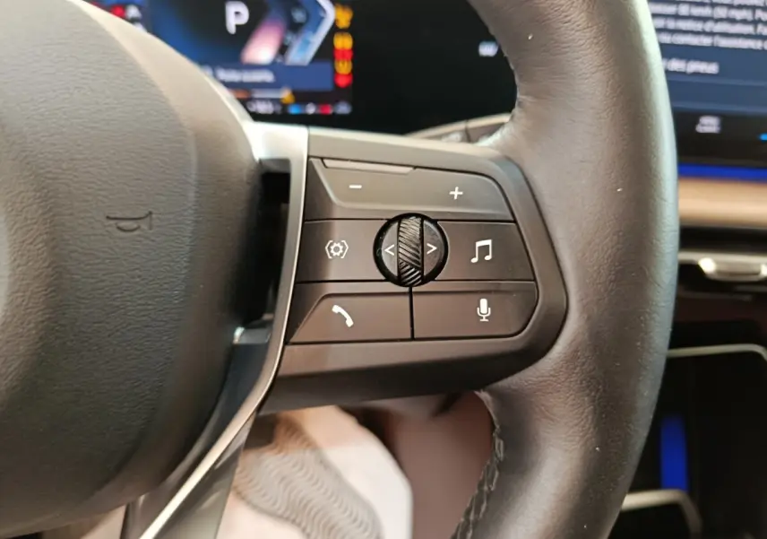 Gros plan sur le volant cuir noir de la BMW X1 2023, avec commandes multifonctions visibles côté droit.