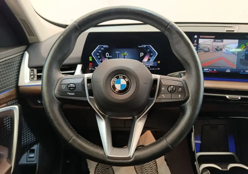 Vue centrée sur le volant cuir noir multifonctions de la BMW X1 2023 avec tableau de bord digital et écran tactile.