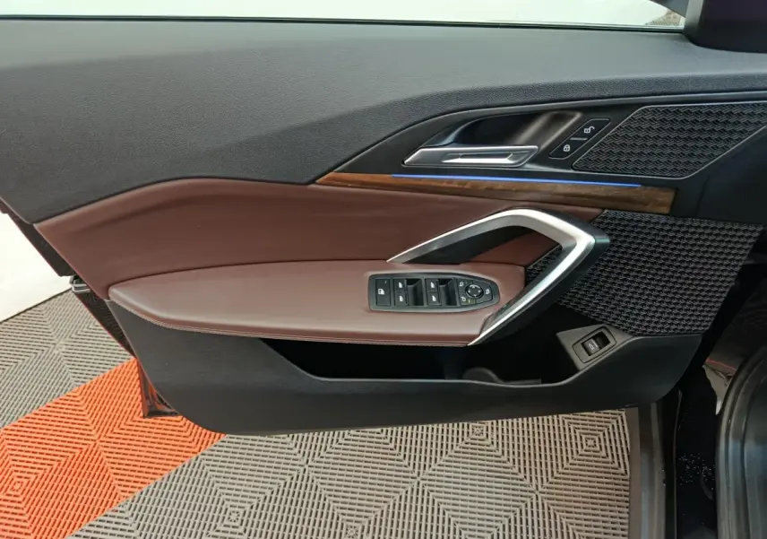 Vue intérieure du panneau de porte côté conducteur de la BMW X1 2023, avec garniture marron et inserts bois et métal.