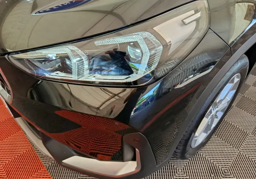 Gros plan sur le phare avant droit d’un BMW X1 noir 2023 avec jante alliage et pare-chocs argenté.