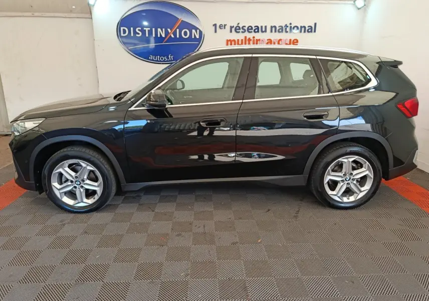 BMW X1 sDrive18i Business Design noir vue de profil côté gauche, avec jantes alliage et toit spoiler visible.