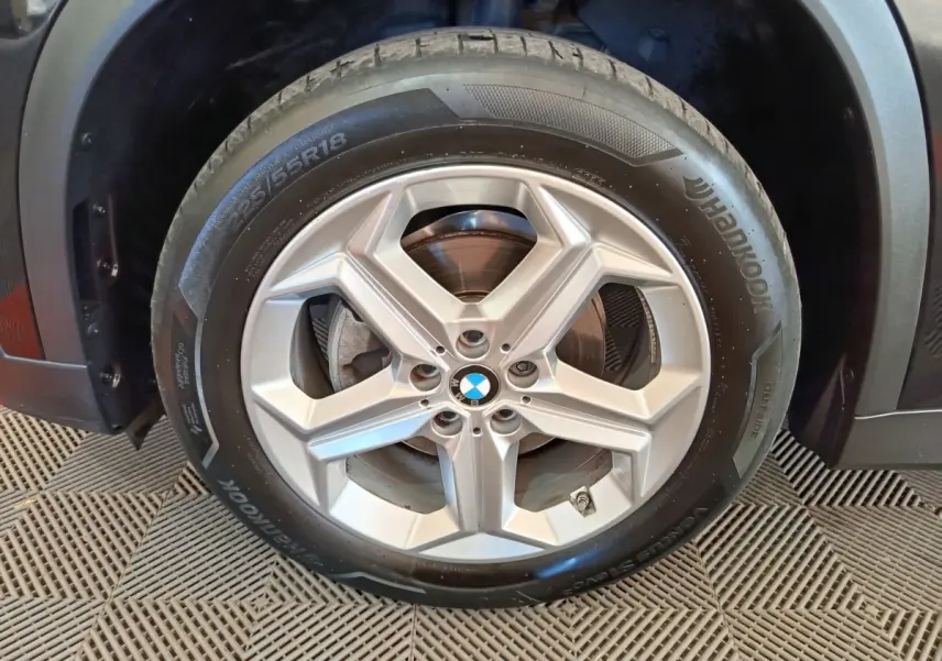 Gros plan sur la roue avant droite avec jante argentée et logo BMW, partie noire du BMW X1 visible en arrière-plan.