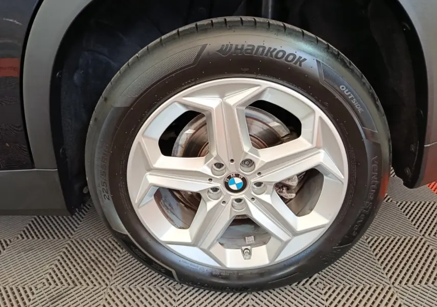 Gros plan sur la roue avant droite avec jante argentée et pneu Hankook du BMW X1 noir 2023.